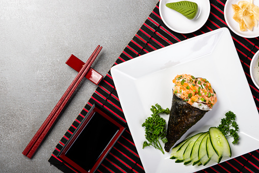 Salmon temaki sushi on black plate on gray background. Japanese cuisine. Top view.