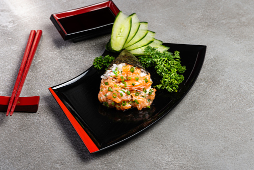 Salmon temaki sushi on black plate on gray background. Japanese cuisine.