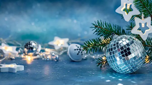 Photo of silver glass ball, jingle bells and glowing star lights garland. green christmas tree branch on blurred blue background