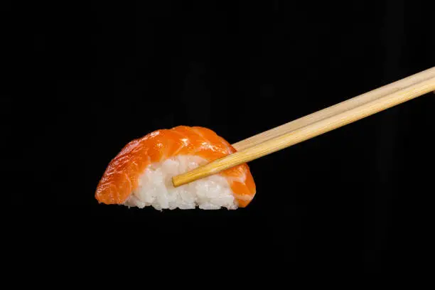 Photo of Nigiri Sushi. Woman picking sushi with chopstick. Black background