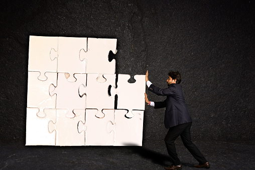 A businessman is putting a piece of puzzle against textured background