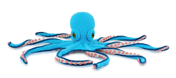 Cute crochet octopus doll isolated on white background with shadow reflection. Playful knitted blue sea devil sitting on white underlay. Plush stuffed puppet octopod toy.
