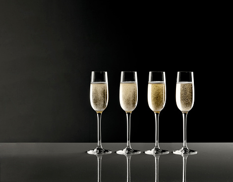 Shot of four full champagne flutes with bubbles on a glass table against black background with copy space
