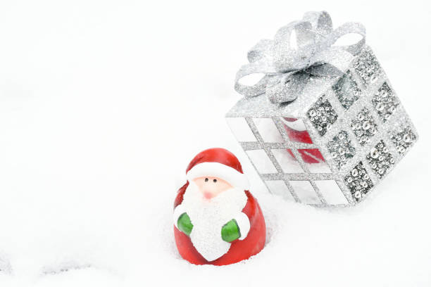 istock Selective focus christmas background with small santa Claus statue  and silver present box on white snow in winter season. Christmas and holiday concept. 1187968193