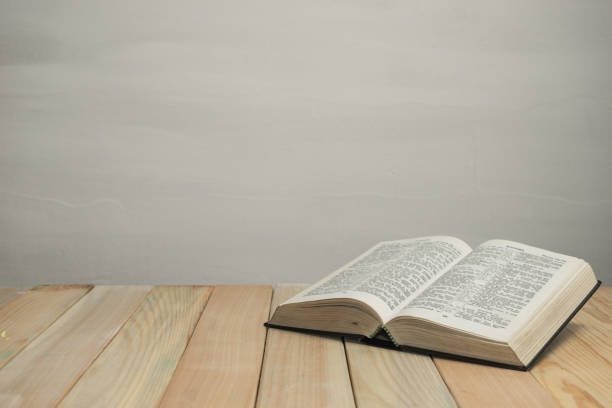 istock Open  Bible on a old wooden table and white wall background. Religion concept. 1187976301