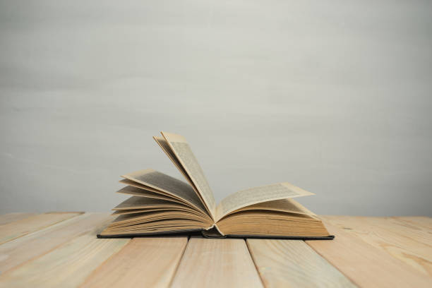 istock Open Old Book on a wooden table and white wall background. 1187976341