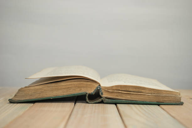 istock Open Old Book on a wooden table and white wall background. 1187976364