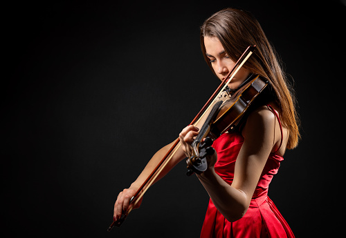 Young violinist woman playing a violin over black background