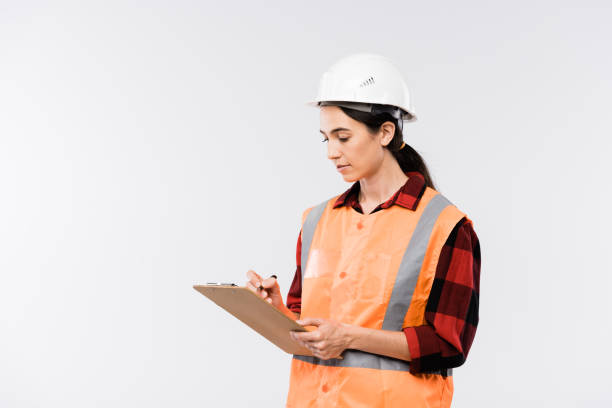istock Female builder in hardhat, flannel and working vest making notes in document 1187980359