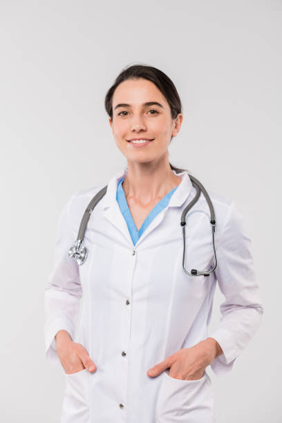 istock Young smiling brunette clinician in whitecoat keeping her hands in pockets 1187980402