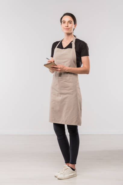 piuttosto giovane cameriera del caffè che prende appunti sull'ordine del cliente in isolamento - grembiule foto e immagini stock