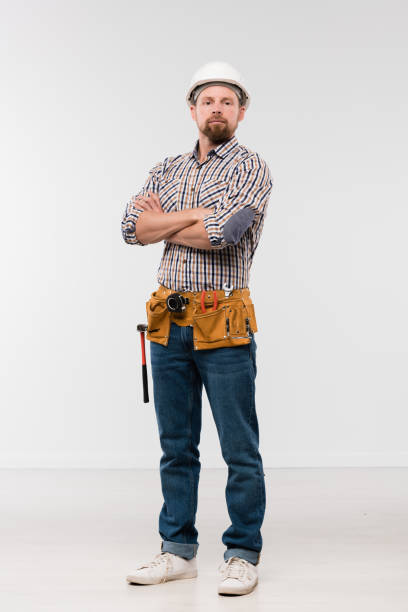 Young successful bearded repairman in white hardhat, jeans and checkered shirt Young successful bearded repairman in white hardhat, checkered shirt and blue jeans standing in front of camera in isolation carpenter portrait stock pictures, royalty-free photos & images