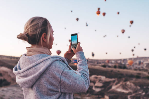 woman taking photo on beautiful landscape and balloons in cappadocia with mobile camera, sunrise time. - anatolya imagens e fotografias de stock