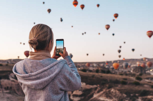 woman taking photo on beautiful landscape and balloons in cappadocia with mobile camera, sunrise time. - anatolya imagens e fotografias de stock