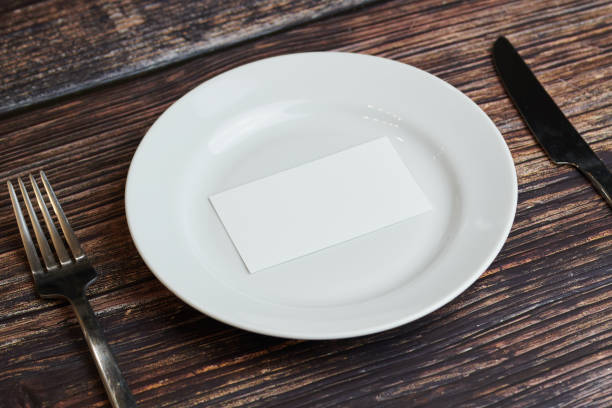 istock Empty plate on table with cutlery and blank business card, top view. Message for visitor of restaurant or cafe. Business lunch without tips concept. 1187998464