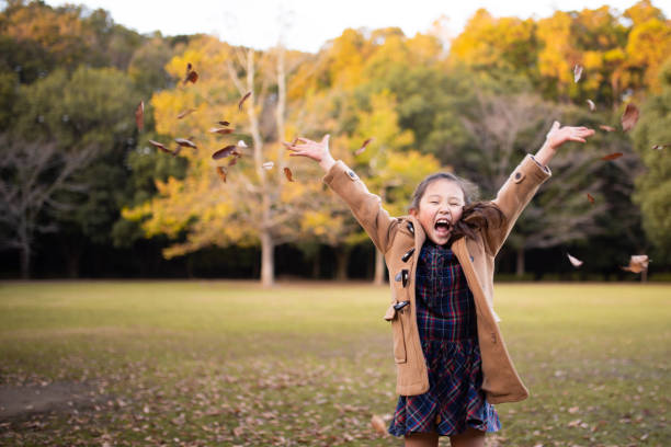 girl playing with fallen leaves - coat warm clothing one person joy imagens e fotografias de stock