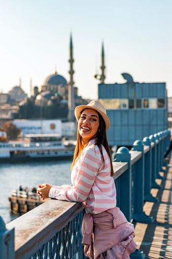 Istanbul the capital of Turkey, eastern tourist city. Young tourist woman on Galata bridge, Golden Horn bay, Istanbul. Ctyscape of famous tourist destination Bosphorus strait channel. Travel landscape Bosporus, Turkey, Europe and Asia.