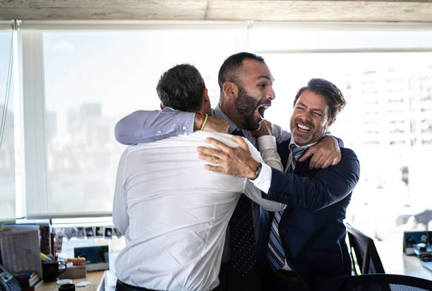 grupo excitado de coworkes que abraçam e que saltam durante uma celebração - office fan - fotografias e filmes do acervo