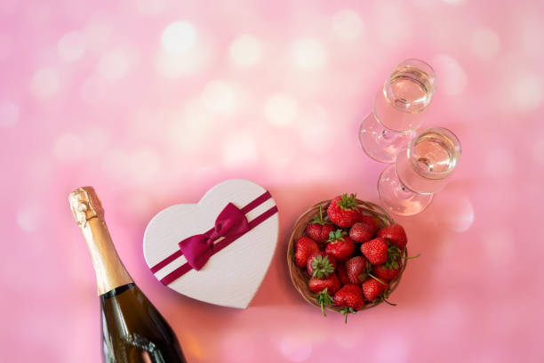 botella de champán, dos copas de champán, caja de gft en forma de corazón y fresa fresca sobre fondo rosa. - champagne pink bubble valentines day fotografías e imágenes de stock