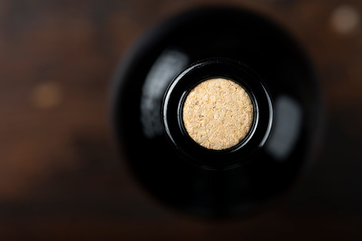 High angle view of a red wine bottle coming from the left top corner beside a wooden handle screw cap leaving a useful copy space on white background. Studio shot taken with Canon EOS 6D Mark II and Canon EF 100 mm f/ 2.8