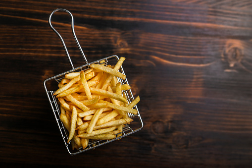 French Fries in a metal basket on a wooden background.