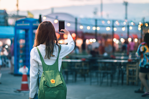 Happy young travel asian woman using mobile phone and selfie on street market against light bokeh background at dusk in Bangkok, Thailand, Travel vacation city concept