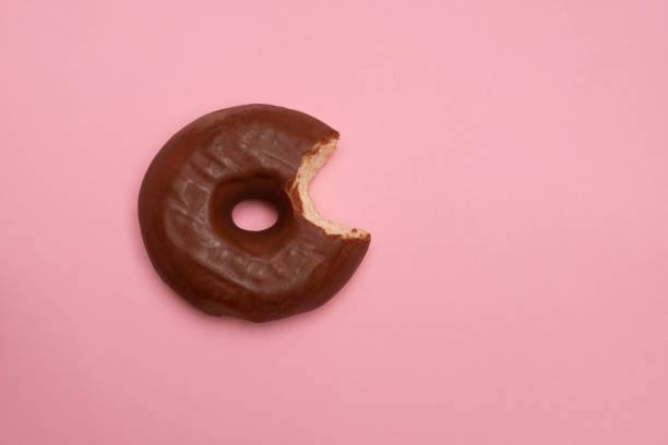 istock Delicious bitten doughnut with chocolate glaze on soft pink paper background 1188016256