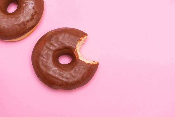 istock Two chocolate frosting donuts with one donut bitten on soft pink background 1188016261