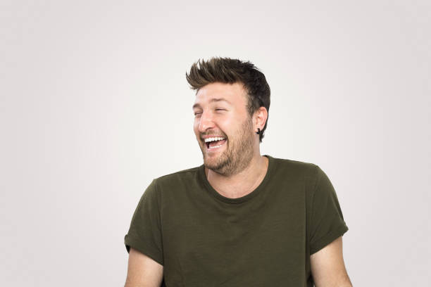 Laughing  handsome young man over isolated  gray background.He standing on isolated background and smile to the camera.Studio shot, isolated background,horizontal composition.Young man wearing green tshirt and he has short and brown hair.