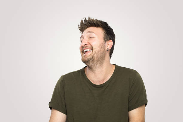 Laughing  handsome young man over isolated  gray background.He standing on isolated background and smile to the camera.Studio shot, isolated background,horizontal composition.Young man wearing green tshirt and he has short and brown hair.