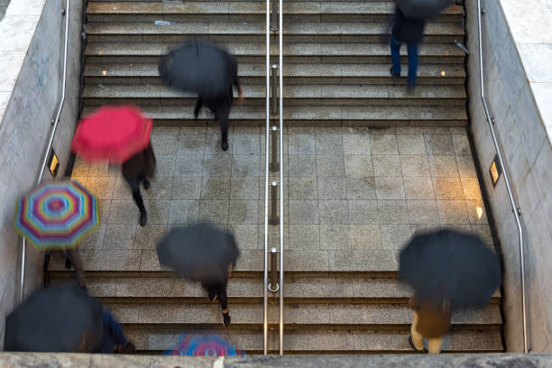 overhead view of people walking towards and away from the entrance to the underground train station under rain with umbrellas - bad weather