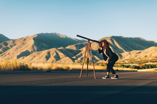 An adult businesswoman dressed in business attire looks through a telescope looking for greater profits for her new business. She is an entrepreneur and loves doing the hard work to find new opportunity. Image taken in Utah, USA.