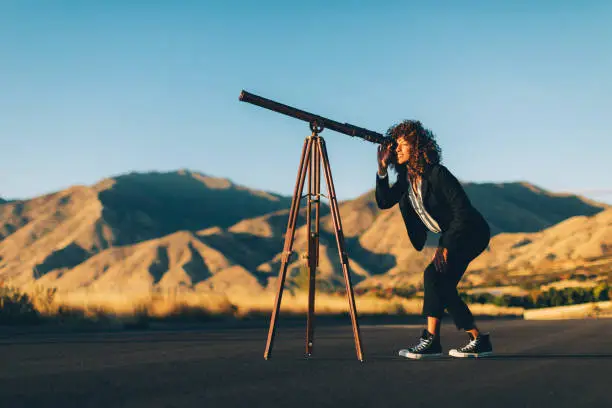 An adult businesswoman dressed in business attire looks through a telescope looking for greater profits for her new business. She is an entrepreneur and loves doing the hard work to find new opportunity. Image taken in Utah, USA.