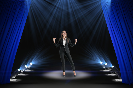 Happy businesswoman on abstract modern stage with spot light and blue curtains. Success, leadership and star concept.
