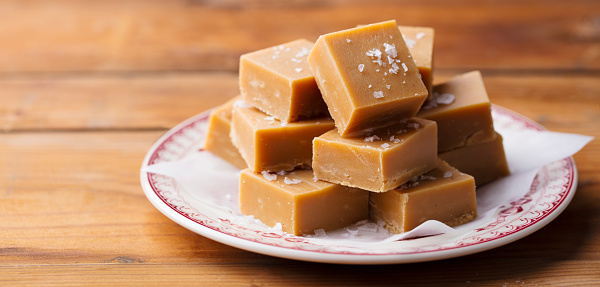 Caramel fudge candies on a plate. Wooden background. Close up