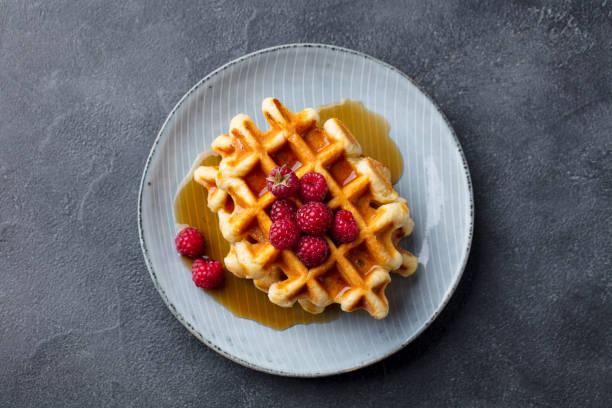 belgische waffeln mit ahornsirup und frischer himbeere. grauer schieferhintergrund. ansicht von oben. - waffle stock-fotos und bilder