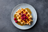 Belgian waffles with maple syrup and fresh raspberry. Grey slate background. Top view.