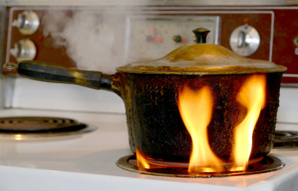 Pot On Fire On Stove An old, covered, charred, blackened pot burning on a burner on an electric stove. The flame is on the outside of the pot rising from the burner. kitchen on fire stock pictures, royalty-free photos & images