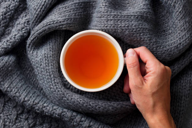 istock Tea cup in female hand on knitted scarf. Grey background. Top view. 1188037238