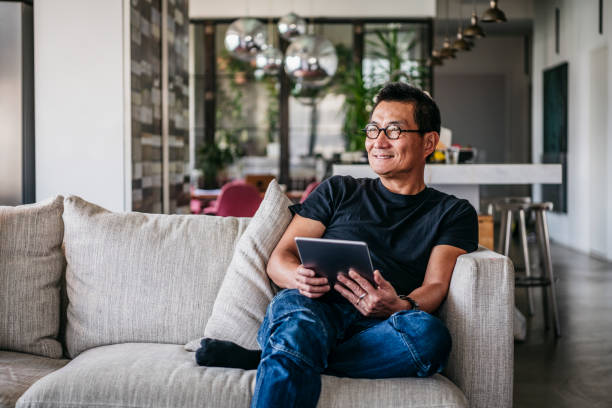 Cheerful Chinese man with tablet looking away and smiling
