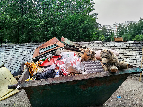 St. Petersburg, Russia - June 9, 2019: Crowded steel dumpster without separate collection of household waste. Soft children's toys thrown in the trash. The photograph was taken in a public, accessible place in the territory where photography is not prohibited.