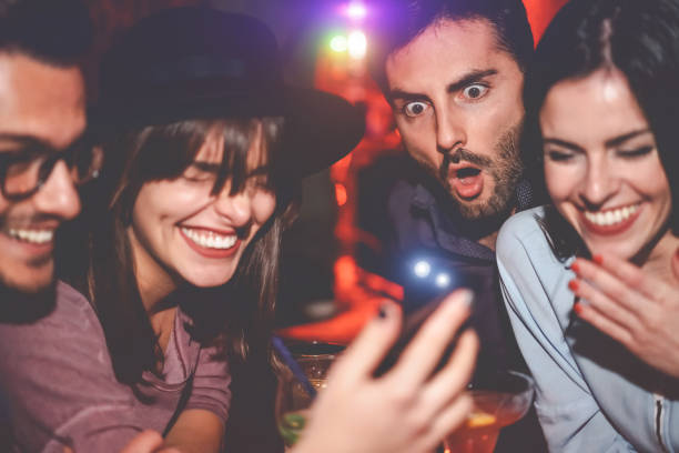 Happy friends having fun watching on mobile smartphone in jazz bar - Group young people using new technology trendy social media apps in club entertainment - Youth millennial and technology concept