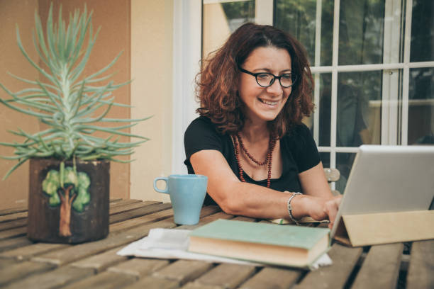 mittelalte frau studieren zu hause mit büchern, zeitung und digitalen tablet-pad. frau liest ein buch und schaut sich videos online auf einem neuen tech-gerät an. bildung, modernes lifestyle- und freizeitkonzept. - women digital tablet outdoors smiling stock-fotos und bilder