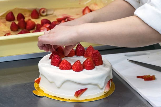 istock Female pastry chef hands, decorating a cream cake with strawberries. 1188056224
