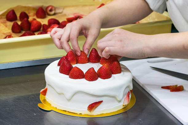 istock Female pastry chef hands, decorating a cream cake with strawberries. 1188056781