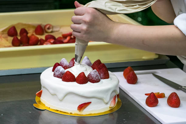 mani da pasticcere donna, decorando una torta di fragole con una manica color crema - cake decorations foto e immagini stock