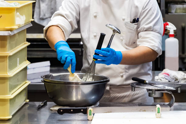 A male pastry chef using a spatula and a whisk while making whipped cream
