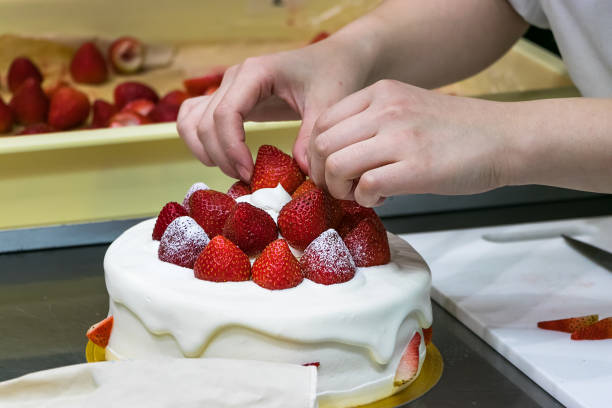 istock Female pastry chef hands, decorating a cream cake with strawberries 1188056950