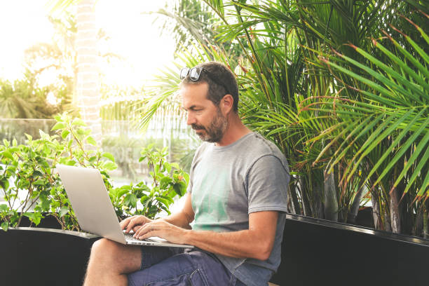 istock Man working with laptop outdoor in a beautiful terrace. Boy using smartphone and computer sitting cross-legged in a dehor in the evening. Home work, business, technology and lifestyle concept. 1188057892