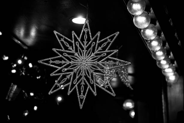 Christmas decor. Winter holiday decorations. Travel Europe in Christmas time. New Year celebration traditions. fotografía en blanco y negro de estrella brillante en forma de adorno de navidad sobre fondo oscuro de luces de navidad. primer plano de estrella de cristal ornamentado de plata. decoración de año nuevo y fila de lámparas de vidrio retro.